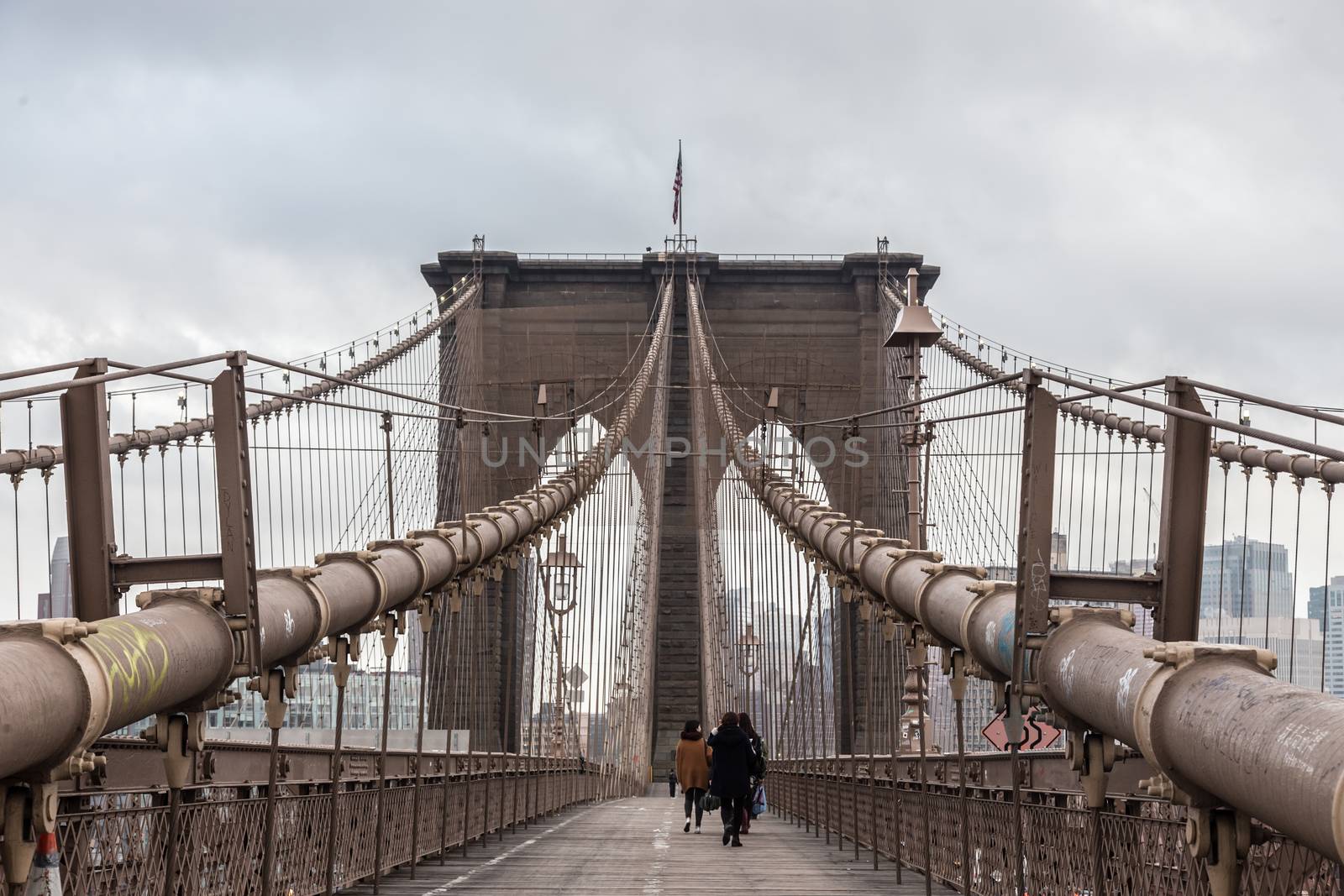 People walking on pedestrian path across Brooklyn bridge. New York City Manhattan downtown with skyscrapers over East River panorama as seen from Brooklyn bridge.