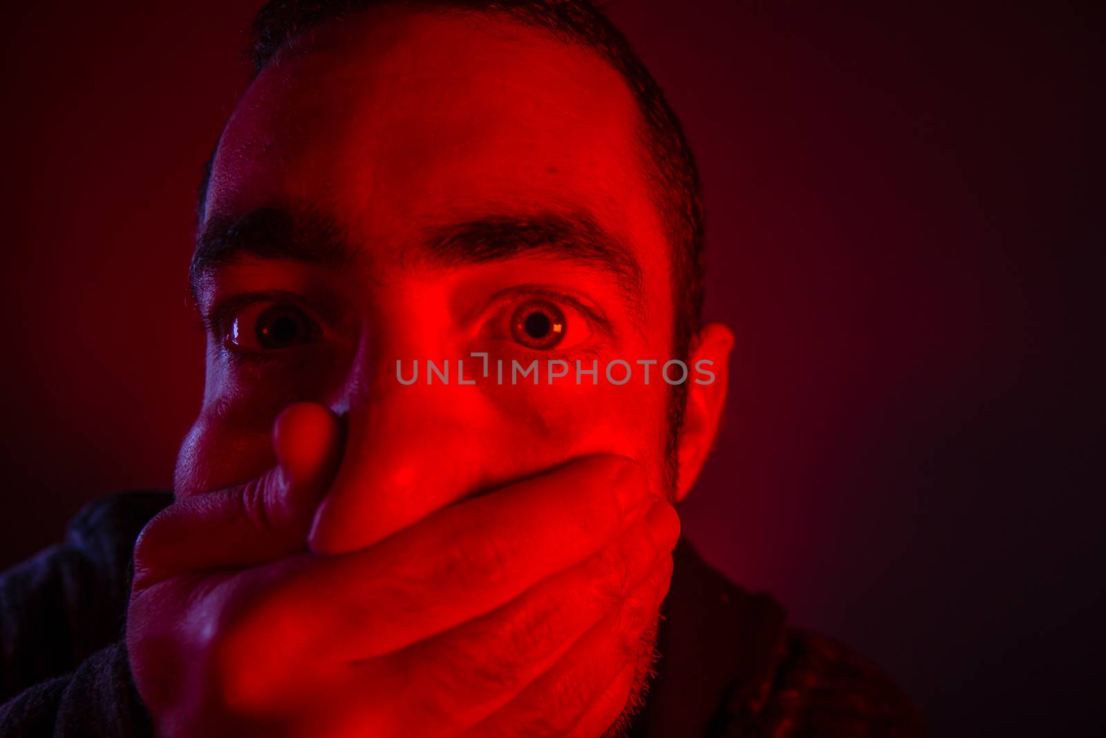 Closeup of a mans hand covering a man mouth with terrified facial expression.