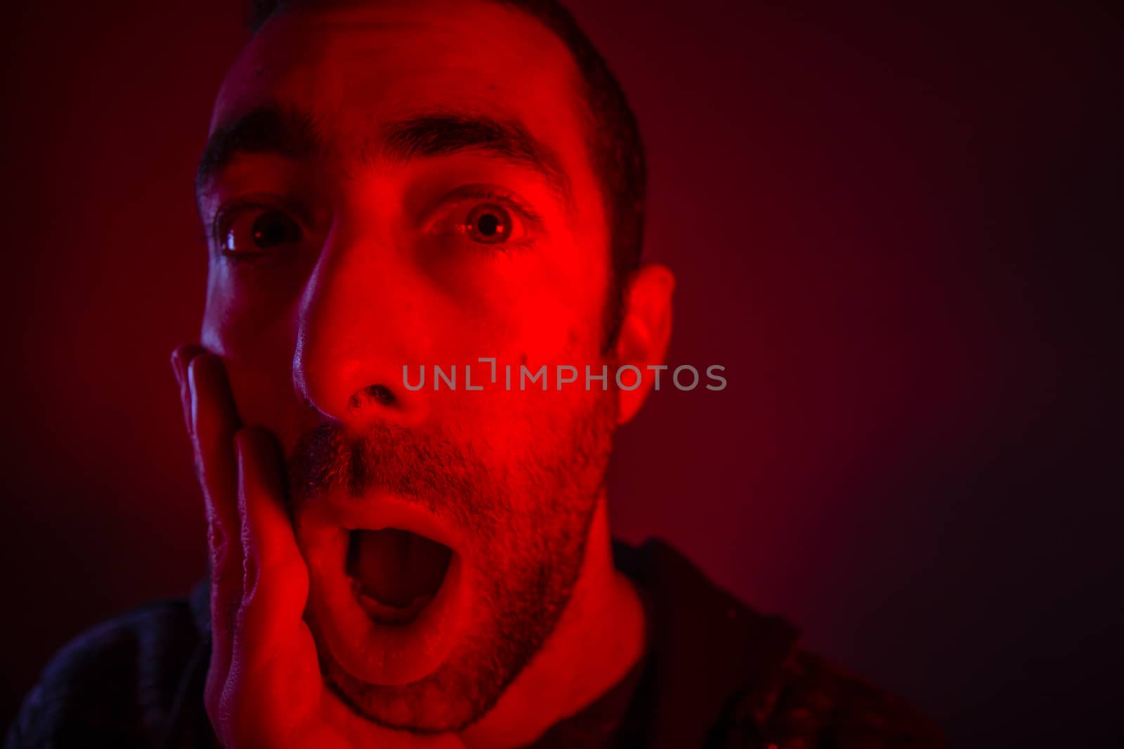 Man with surprised facial expression with opened mouth. Close up headshot portrait of shocked man with his hand on the face.