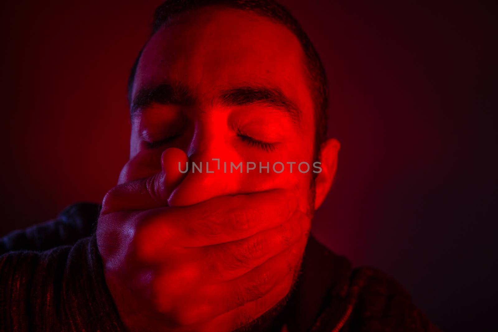 Closeup of a mans hand covering a man mouth with terrified facial expression.