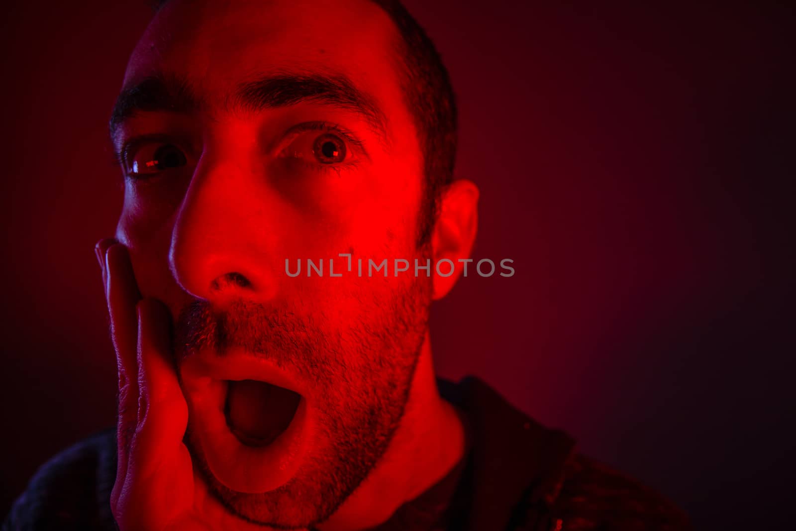 Man with surprised facial expression with opened mouth. Close up headshot portrait of shocked man with his hand on the face.