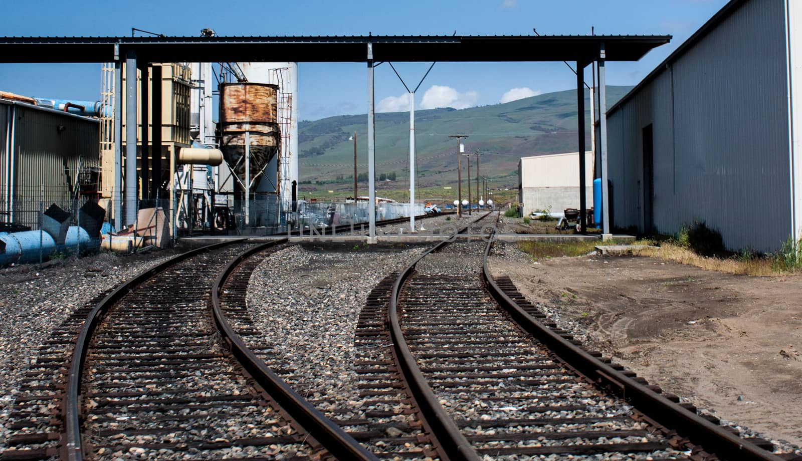 2 railroad tracks leading in to a loading unloading facility with an overhead awning