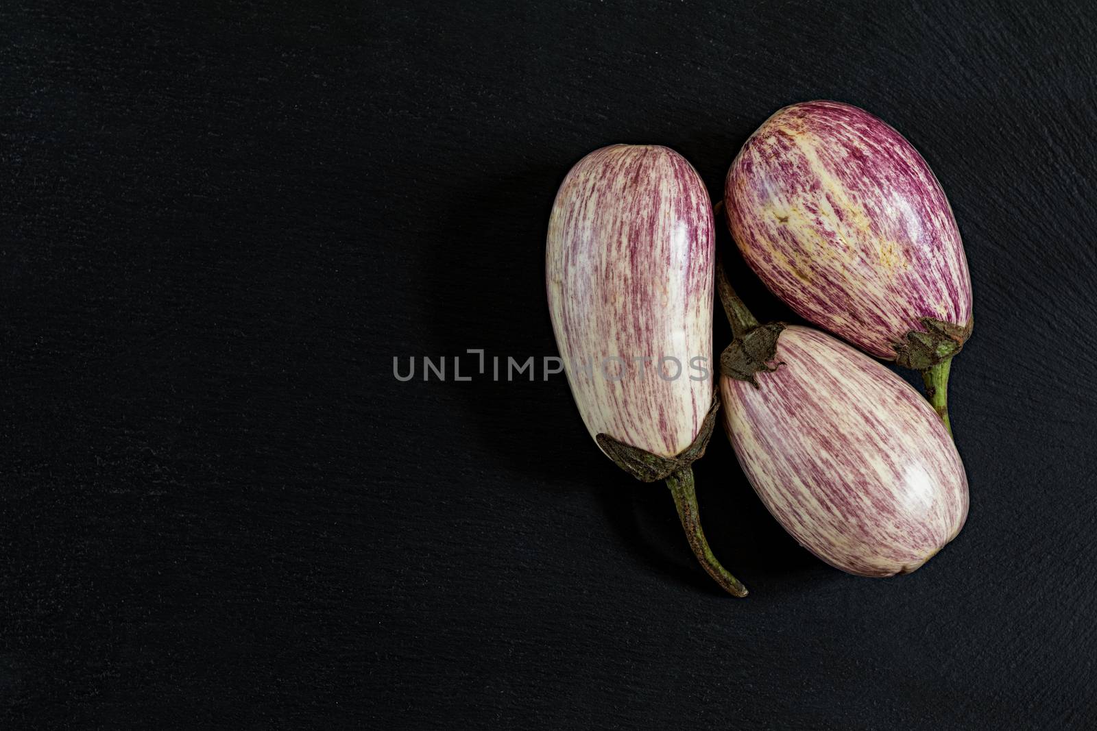 Purple graffiti three eggplants on black stone surface. Top view, copy space.