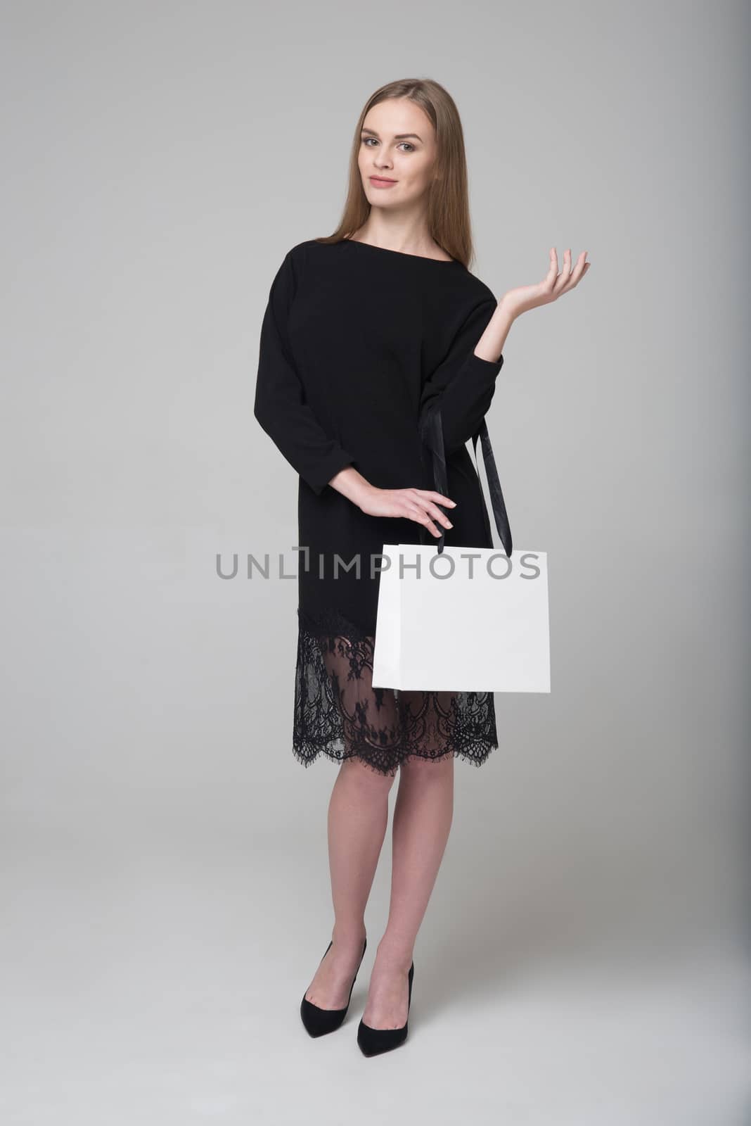 Young beautiful long-haired girl in black dress poses with white paper bag for shopping