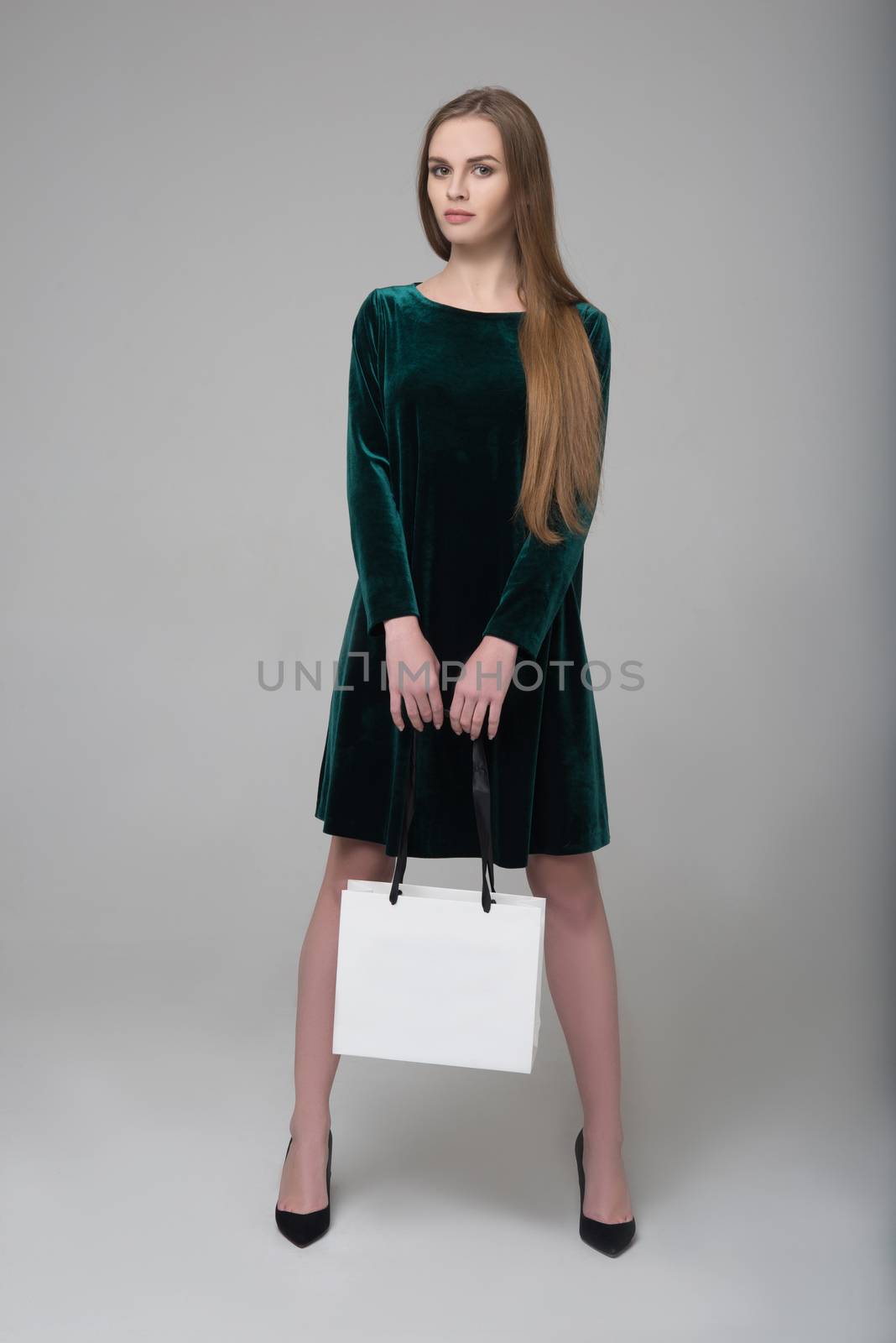 Young beautiful long-haired girl in dark green dress poses with white paper bag for shopping