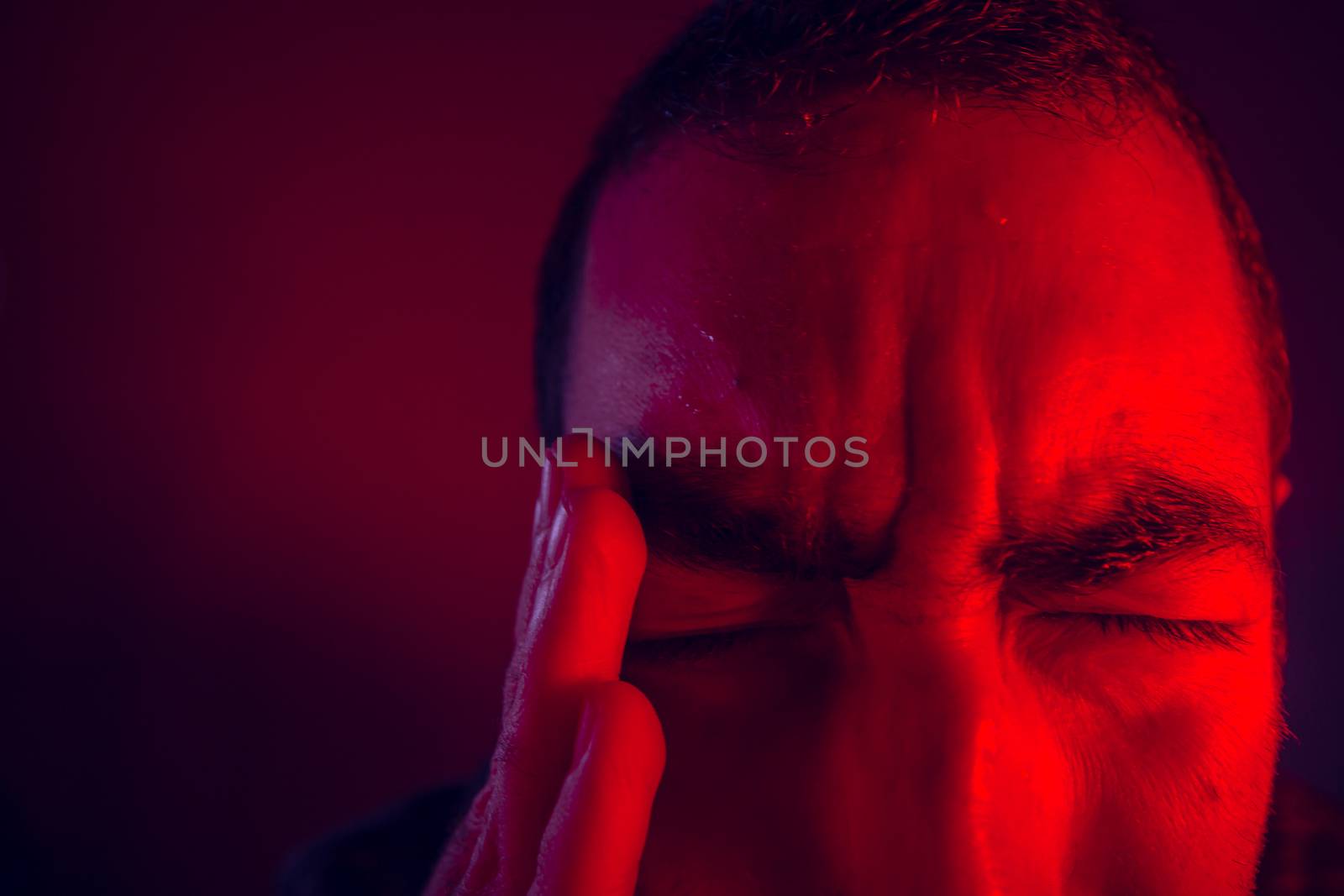 Man is suffering in pain from headache. Close up headshot portrait of man feeling upset or in pain. He touches his head with his hand.