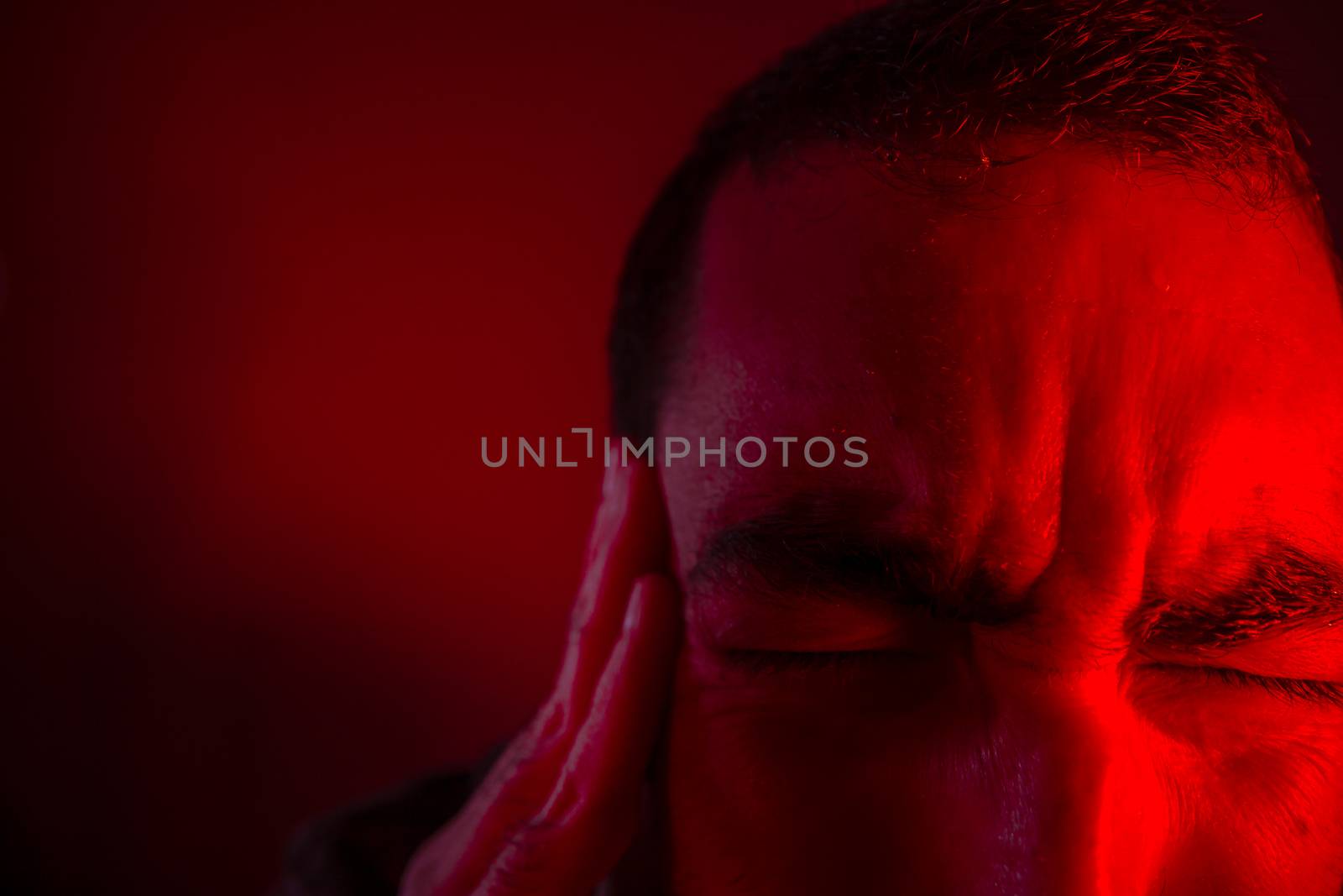 Man is suffering in pain from headache. Close up headshot portrait of man feeling upset or in pain. He touches his head with his hand.