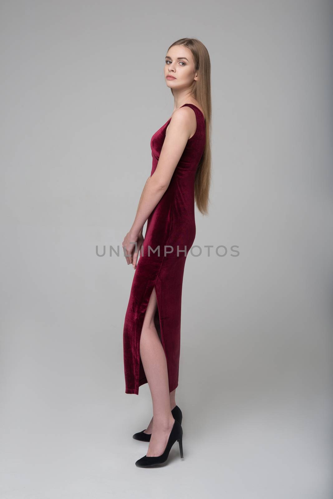 Young beautiful long-haired female model poses in long red dress on grey background