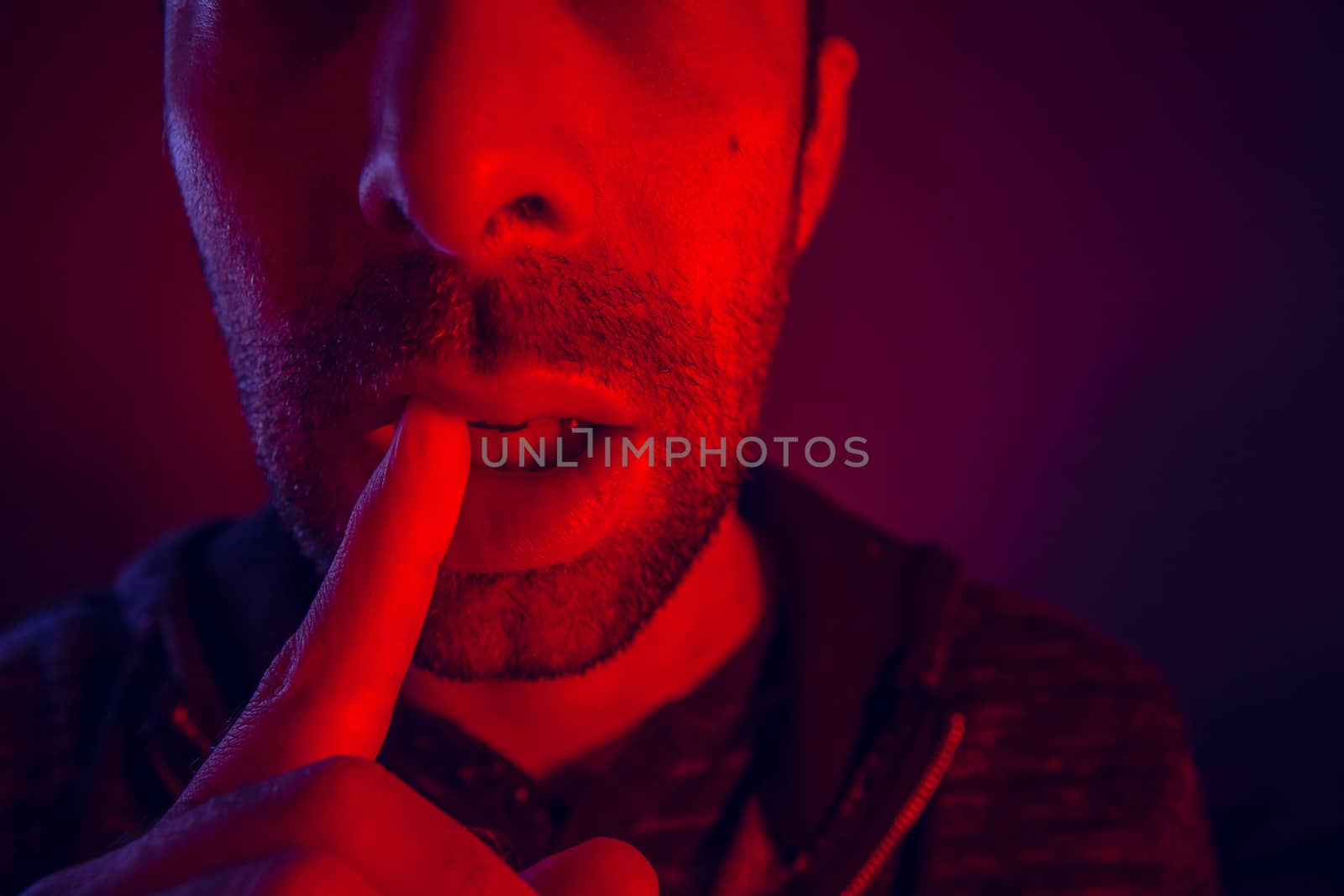 Man with seductive facial expression holding finger on mouth. Close up portrait of flirty young man with shushing gesture with his finger to his lips looking at camera.