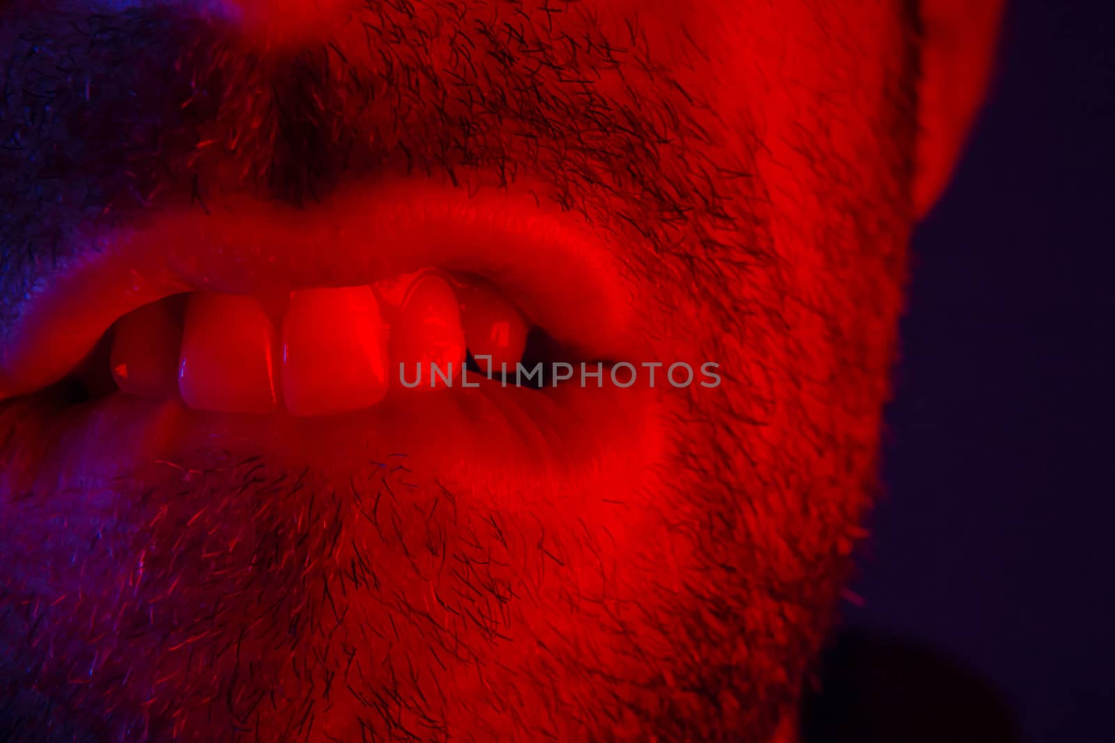 Macro close up on man with seductive facial expression biting his lips. Portrait of flirty young man looking at camera.