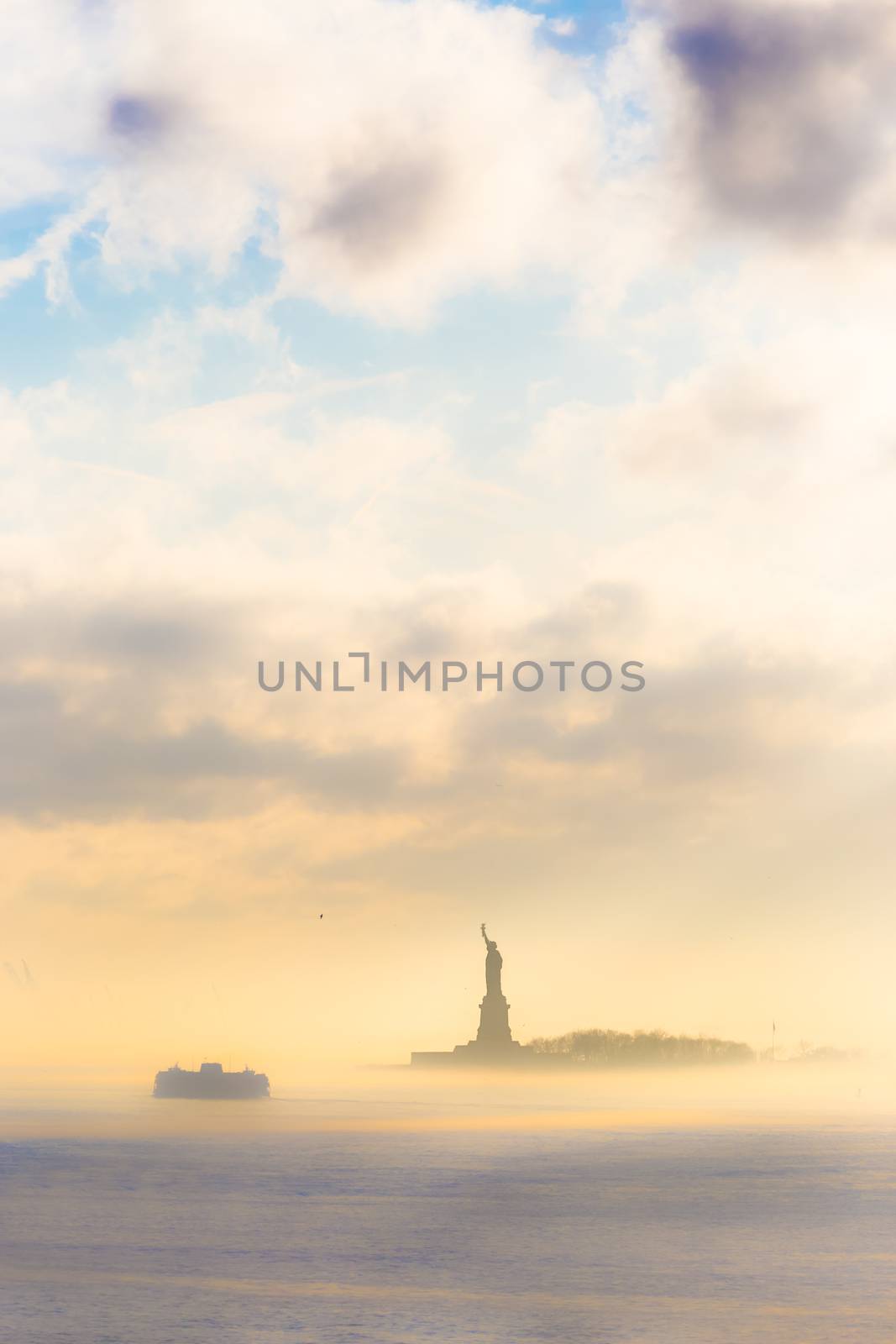 Staten Island Ferry cruises past the Statue of Liberty on a misty sunset. Manhattan, New York City, United States of America. Vertical composition. Copy space.