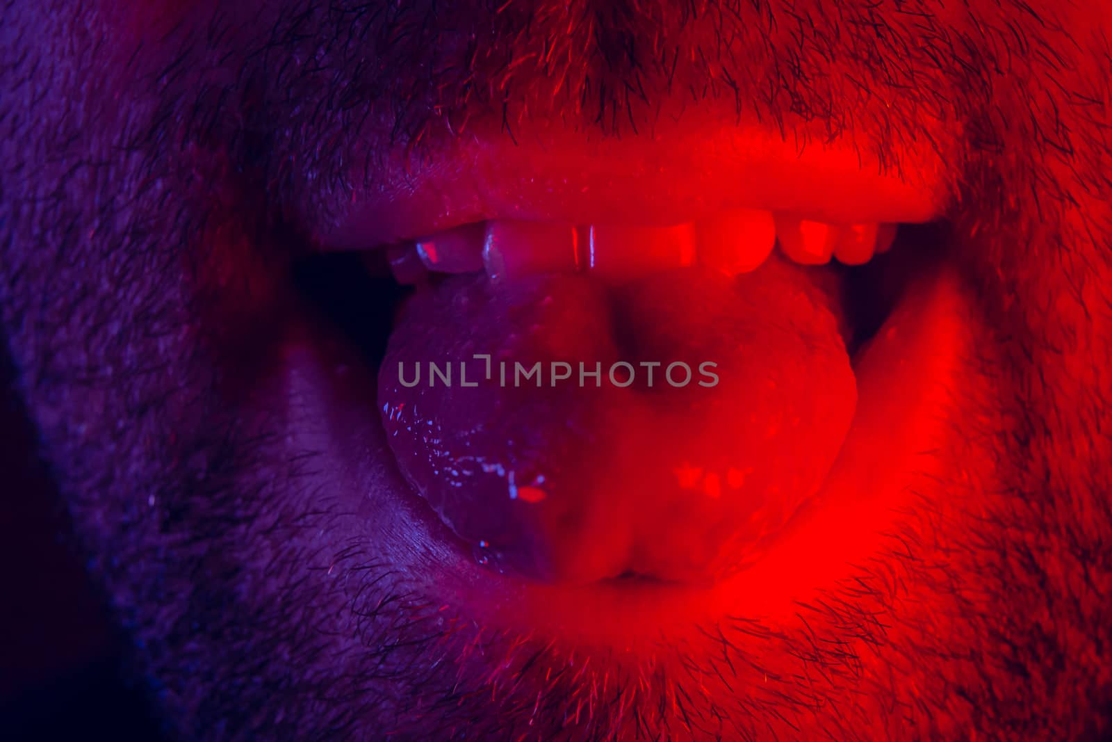 Macro close up on man with happy smiling facial expression sticking out his tongue. Portrait of happy young man looking at camera.