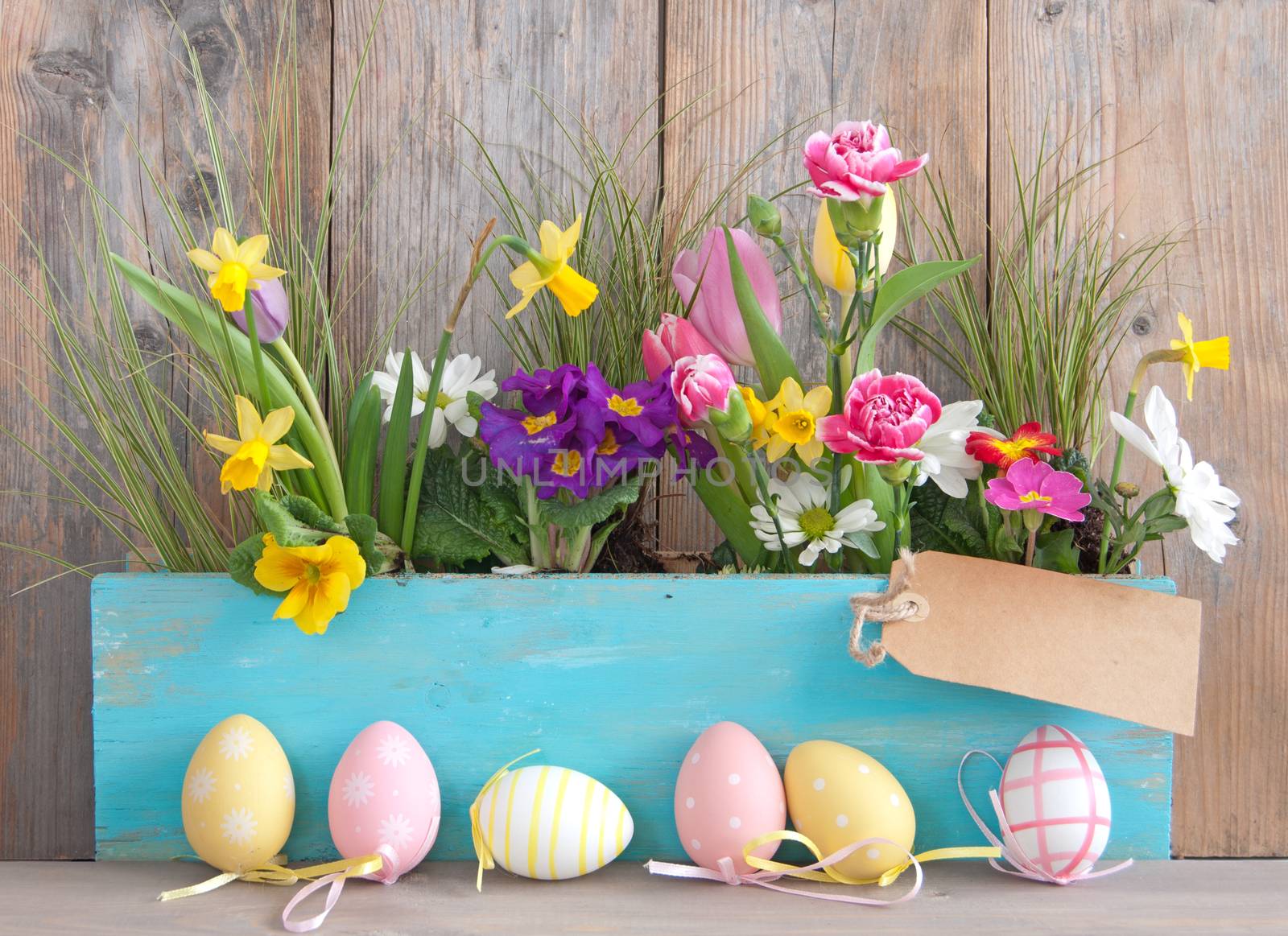 Spring flowers in a wooden pot with row of easter eggs and blank label