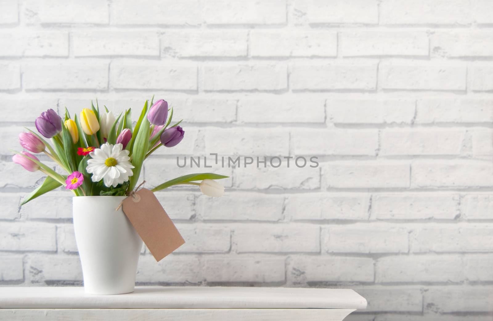 Selection of tulips and daisies inside a pot on top of a fireplace mantelpiece with label