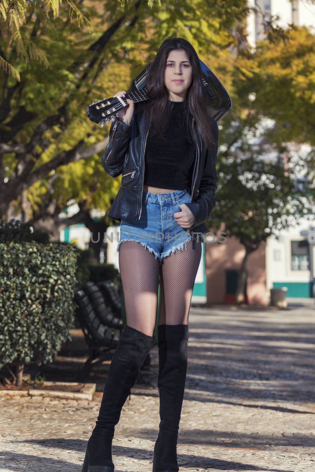 Close view of a beautiful young woman with classic guitar on a garden in the city.