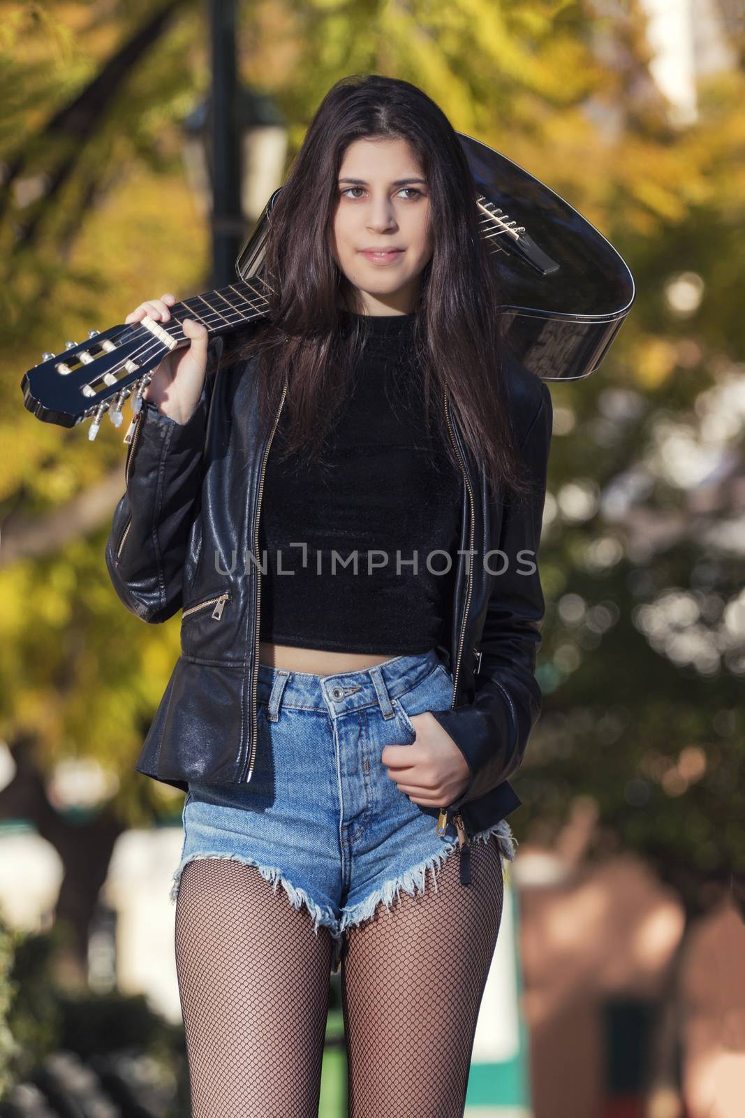 Close view of a beautiful young woman with classic guitar on a garden in the city.