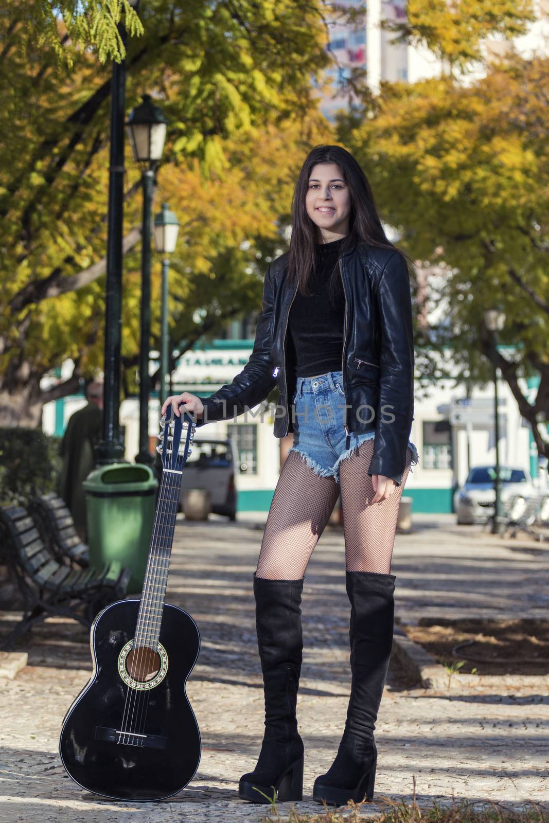 Close view of a beautiful young woman with classic guitar on a garden in the city.