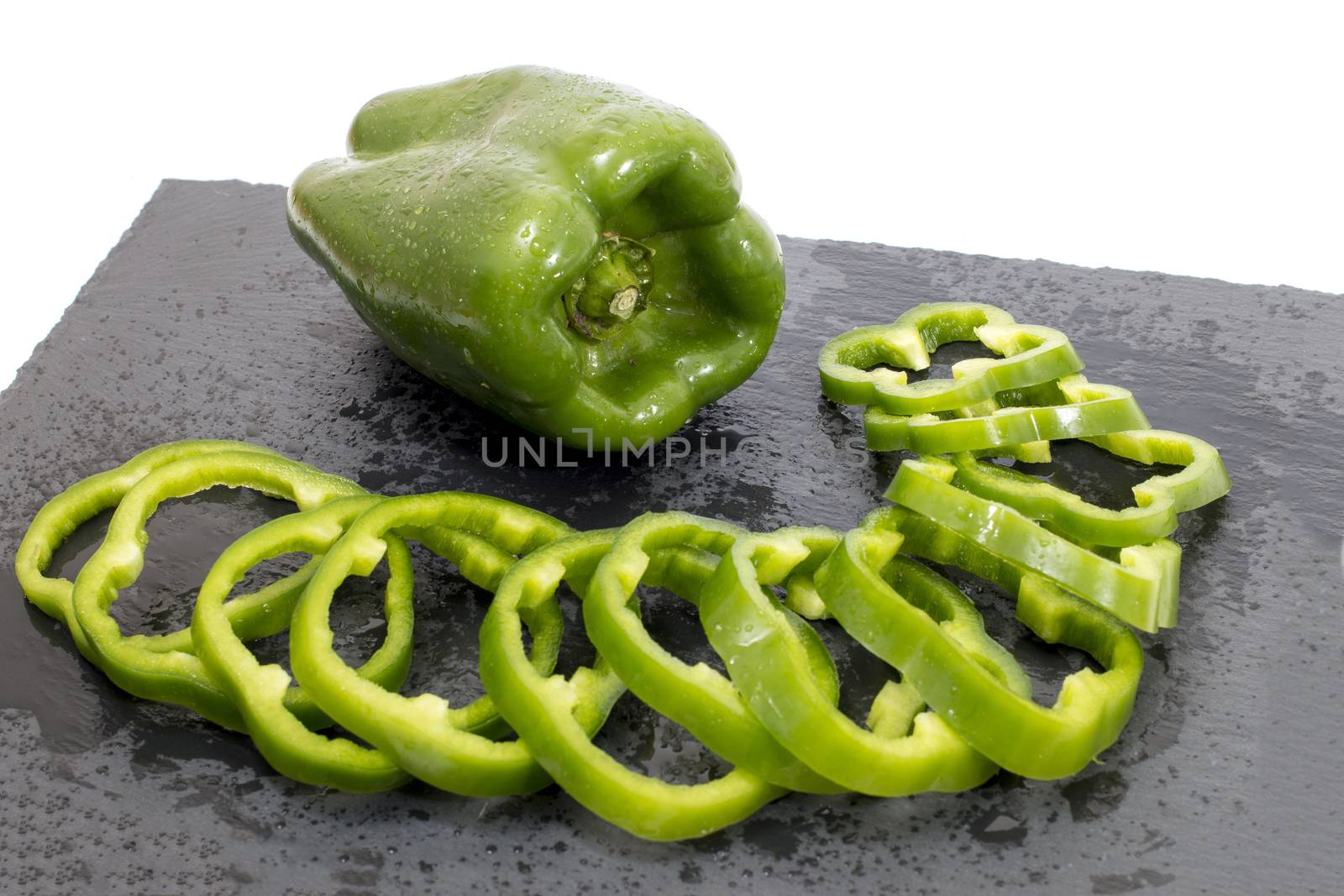 green bell peppers on a black stone of schist, wet and sliced.