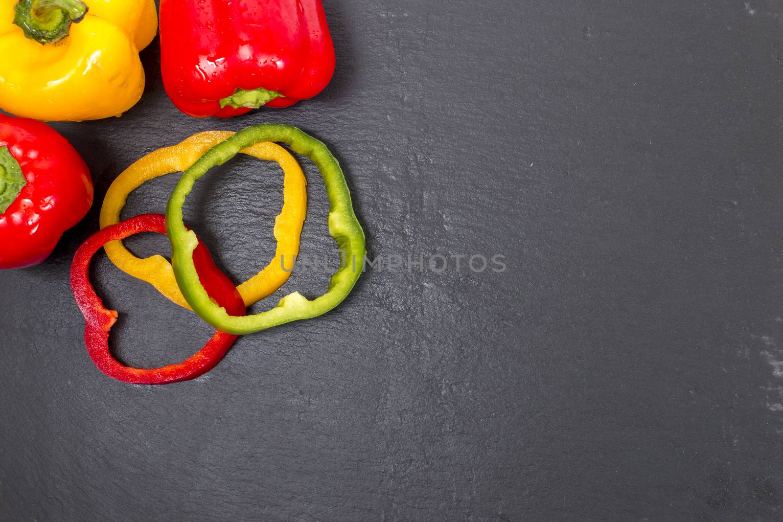 colorful sliced bell peppers on a black stone of schist, wet and organized.