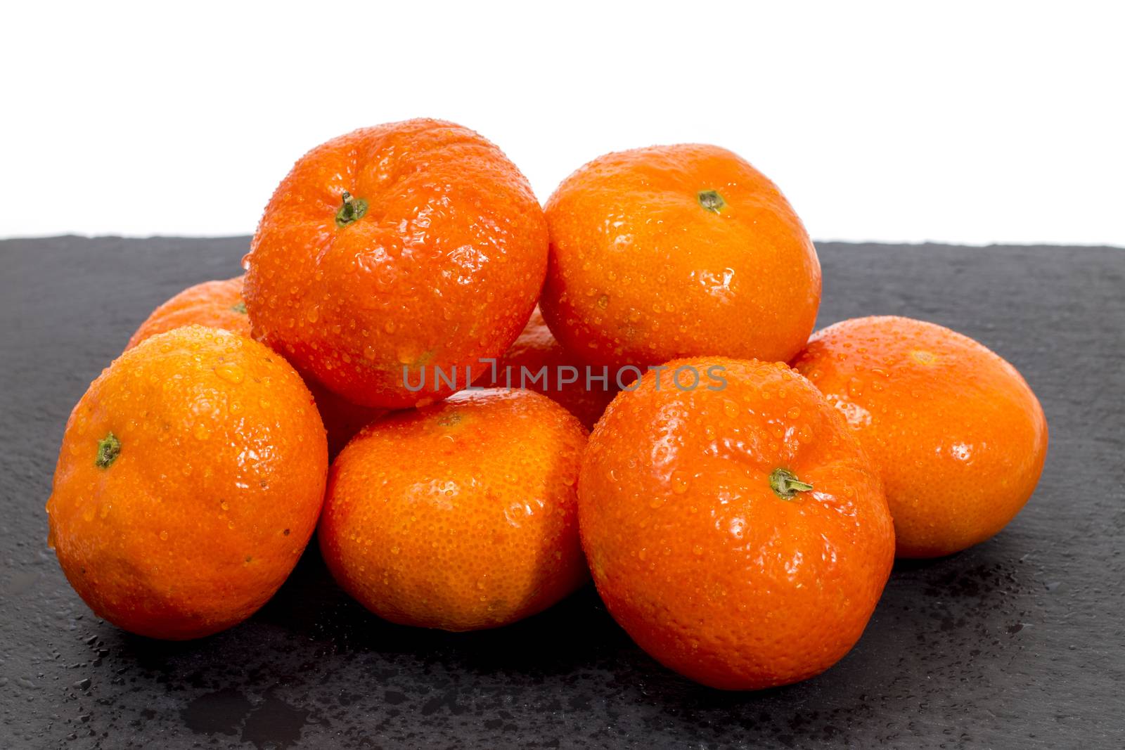 Wet clementines fruits on a black slab of schist.