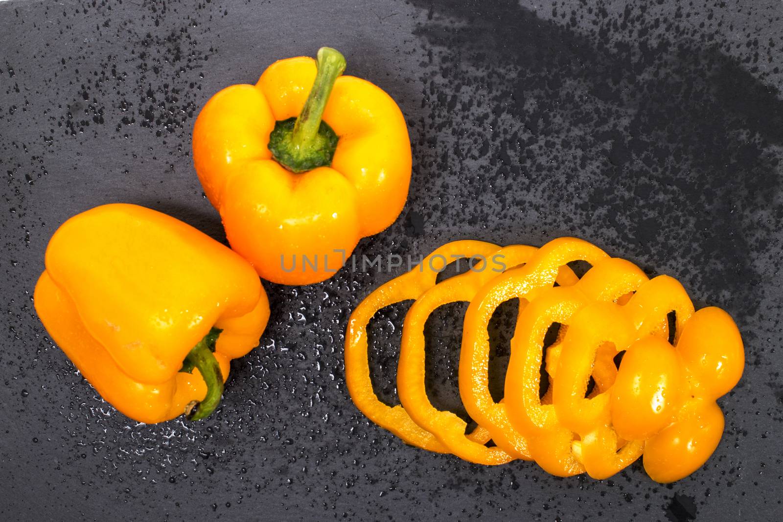 yellow bell peppers on a black stone of schist, wet and sliced.