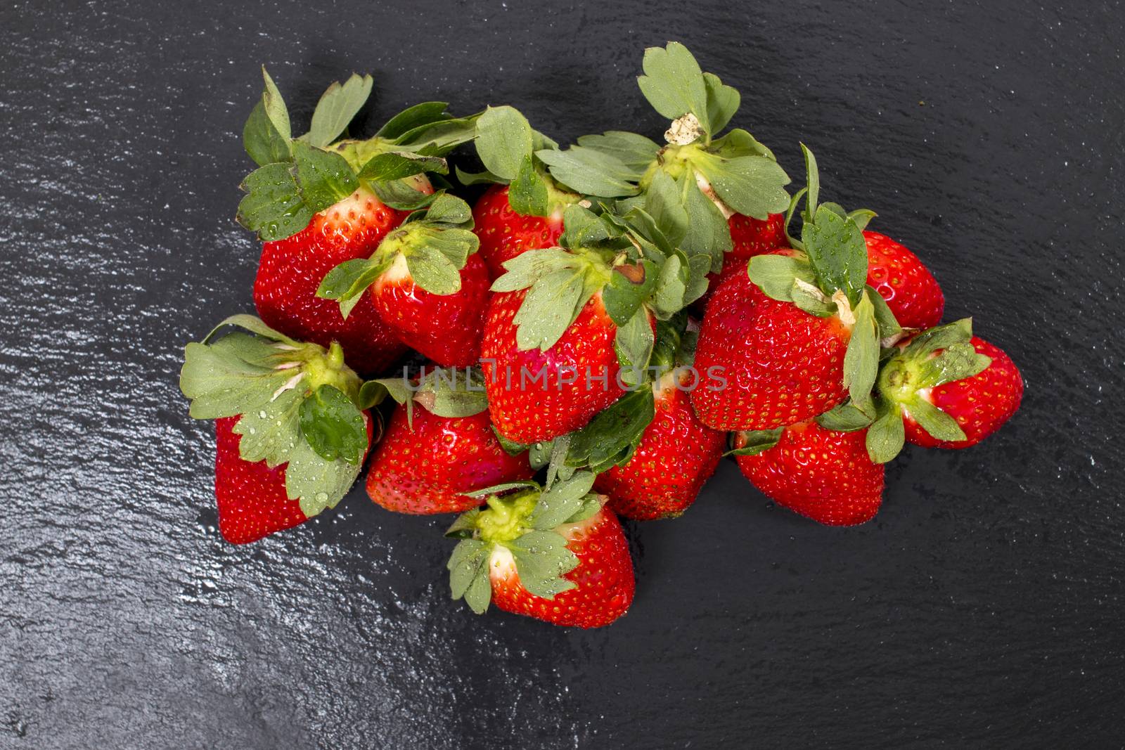 Red tasty strawberries on a black slab of schist.