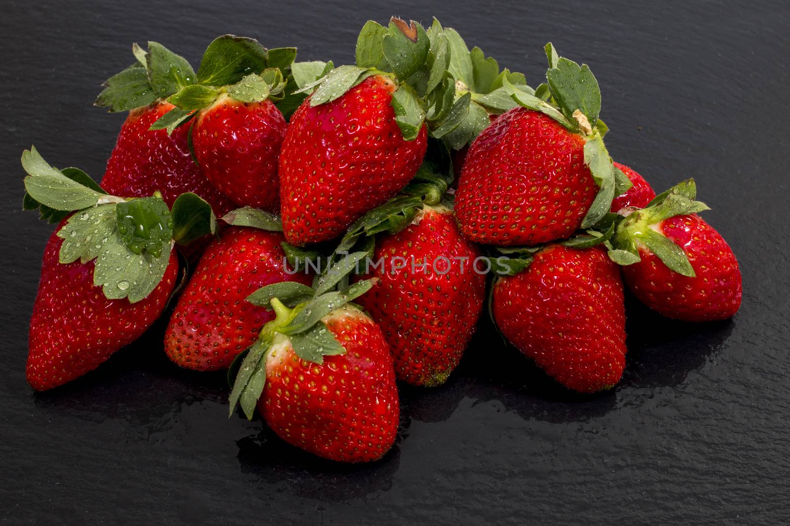 Red tasty strawberries on a black slab of schist.