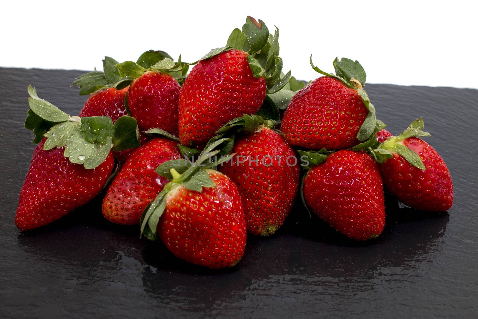 Red tasty strawberries on a black slab of schist.