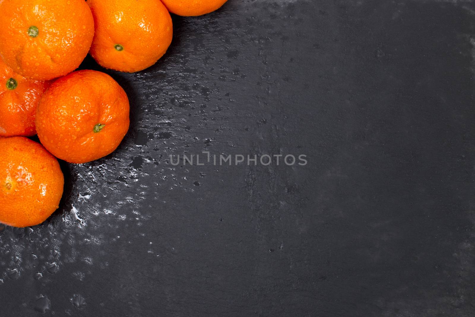 Wet clementines fruits on a black slab of schist.
