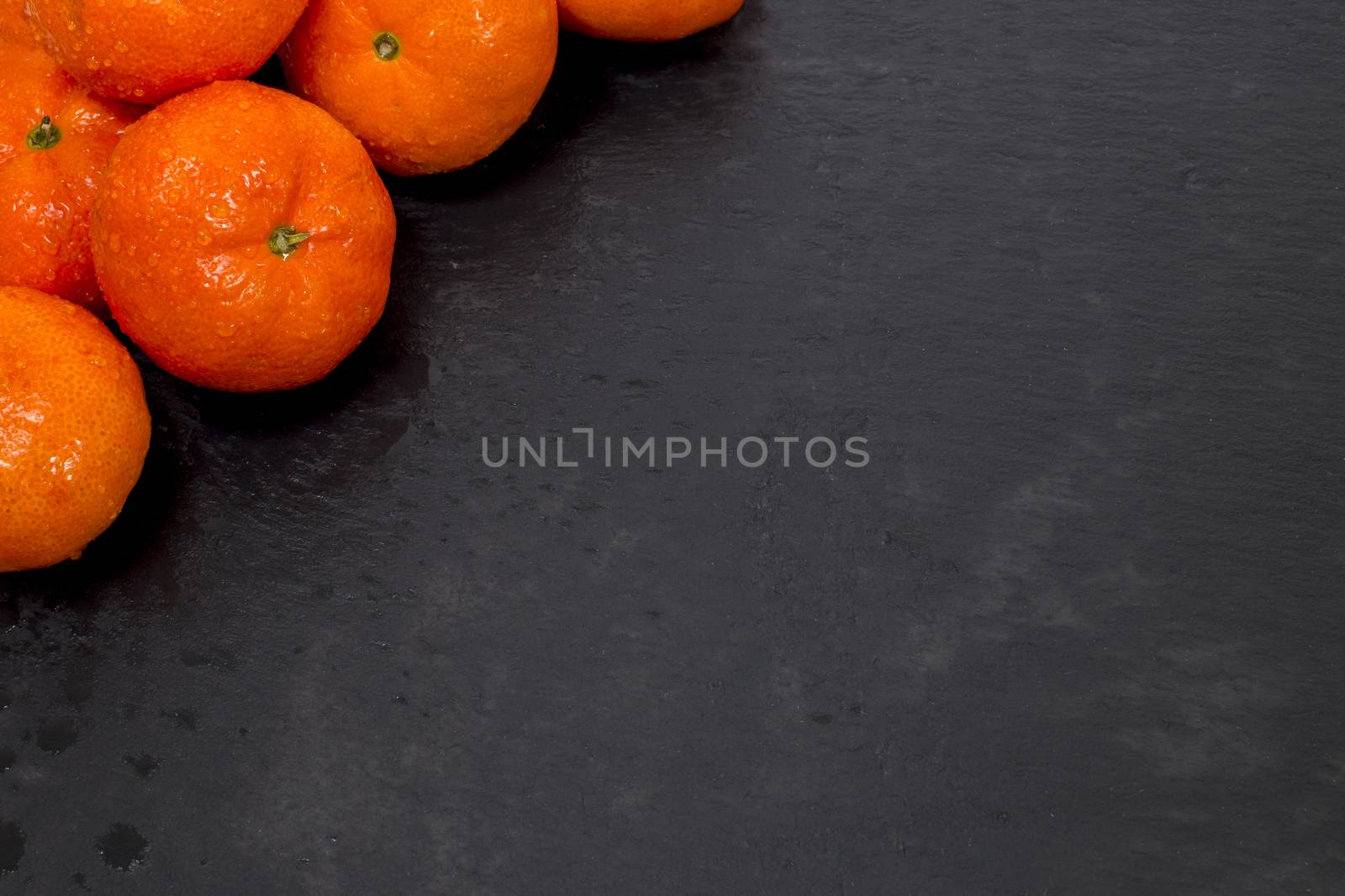 Wet clementines fruits on a black slab of schist.