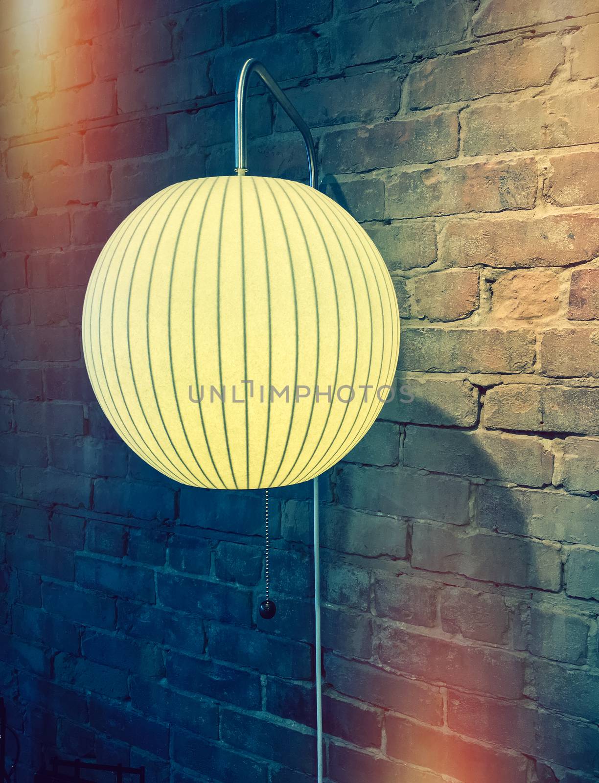 Lamp with round lampshade on brick wall. Retro style image with light leaks.