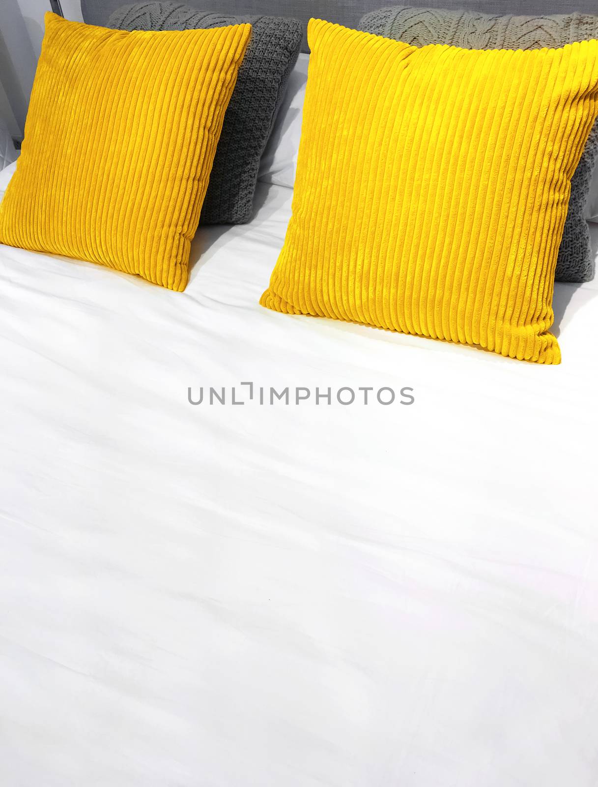 Bed with bright yellow velveteen cushions and white bed sheets.