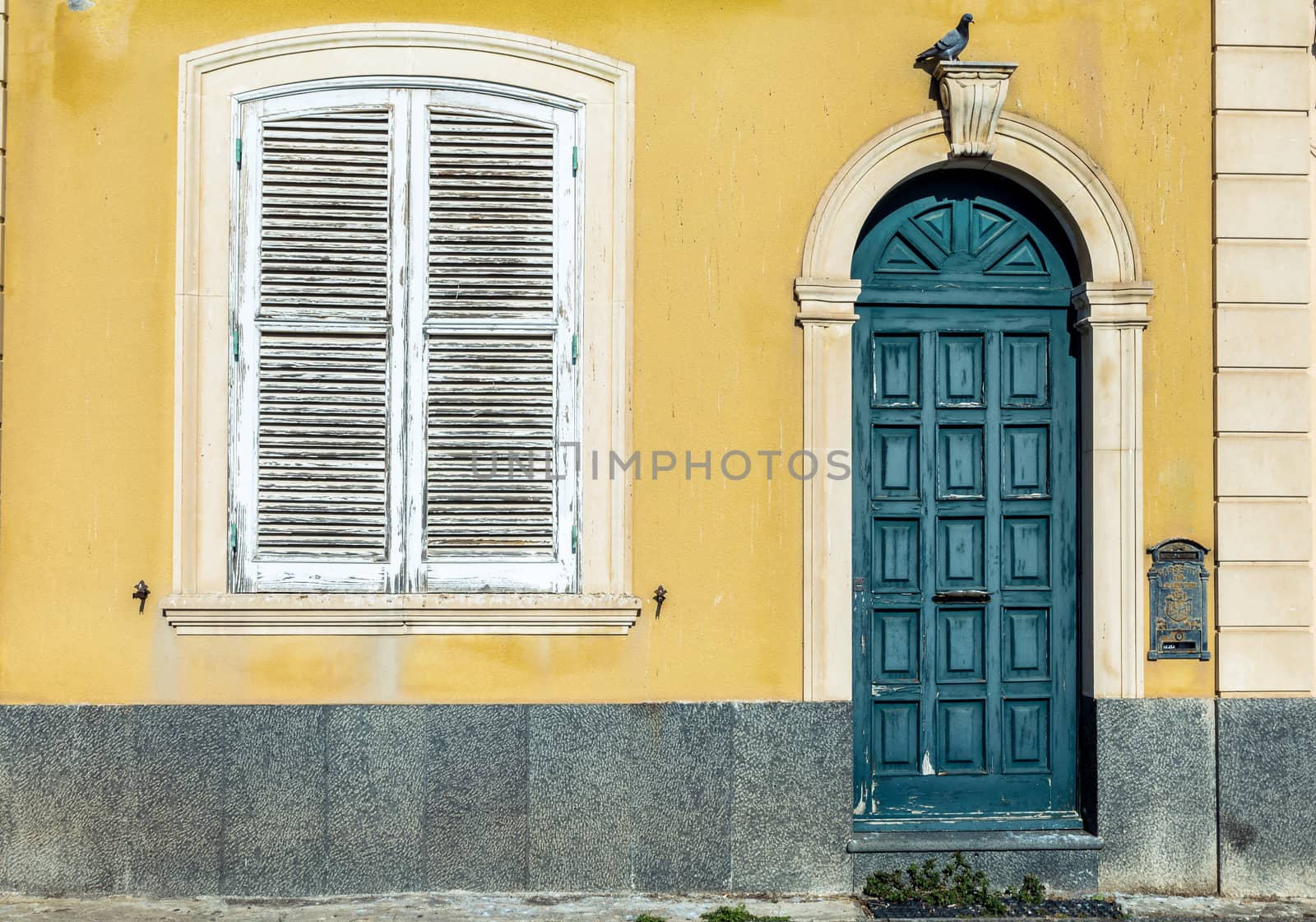 the green door and the white window in an ancient yellow wall