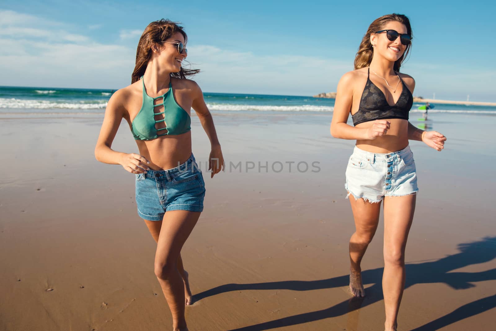 Two beautiful female friends in bikini running at the beach and having fun together