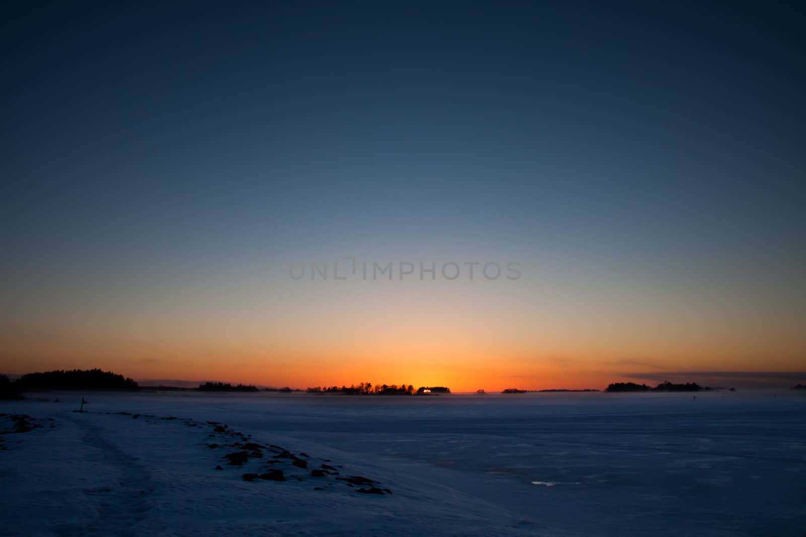 Sunset landscape in cold winter weather. Frozen sea and islands.
