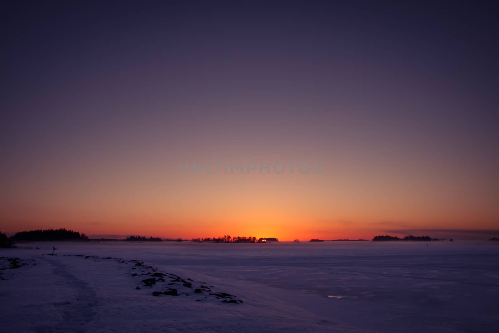 Sunset landscape in cold winter weather. Frozen sea and islands.