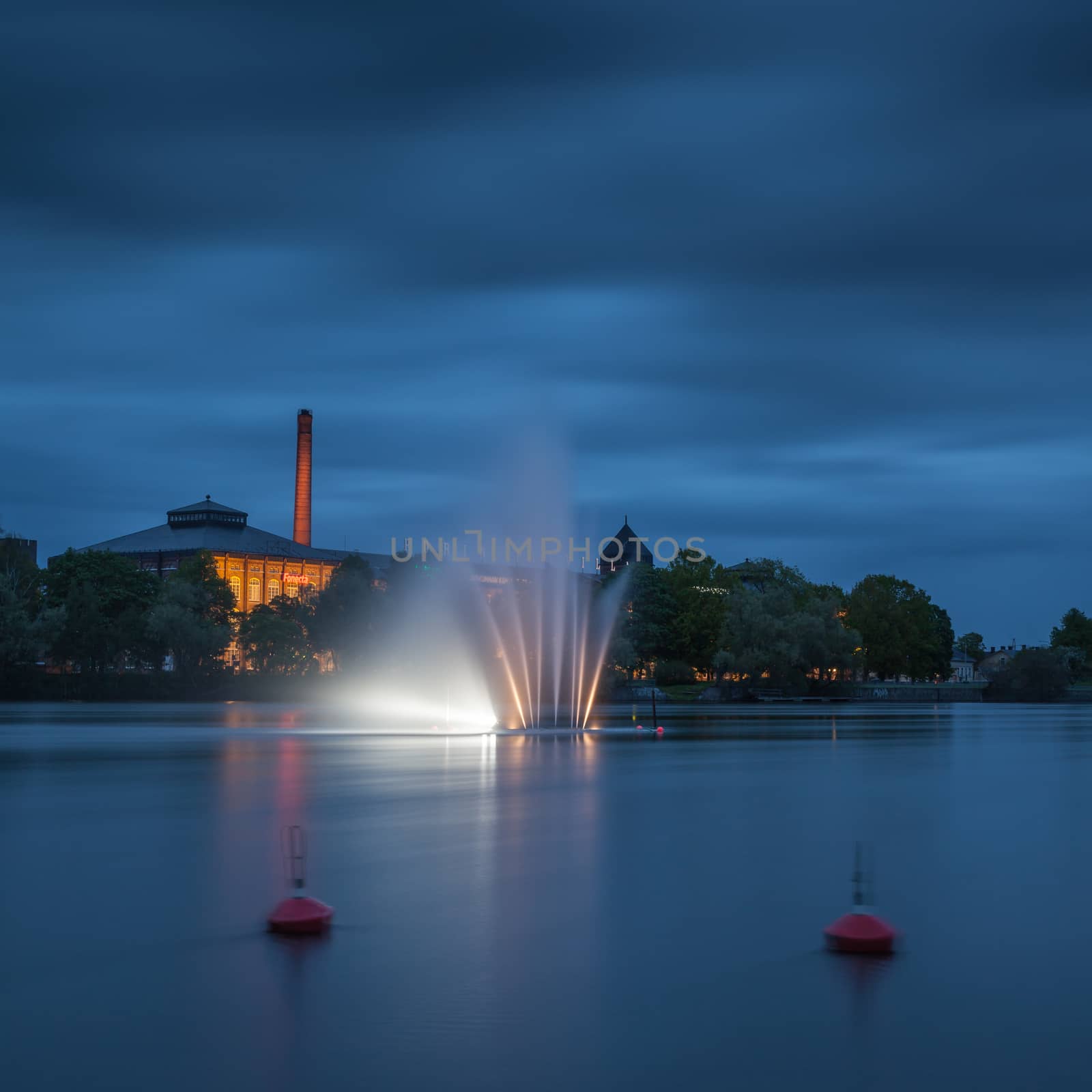 Night landscape with a fountain in the middle of the river. On the back is a former cotton mill.