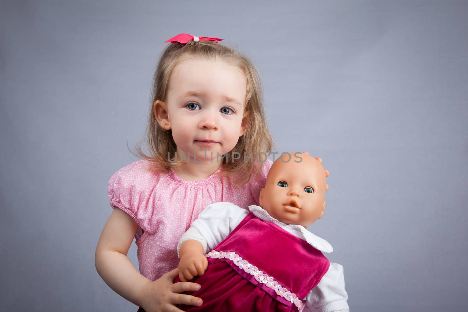 Portrait of the cute girl with a doll. Gray background.