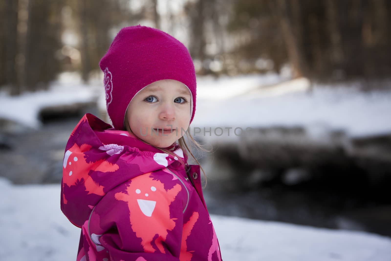 A winter portrait of a young girl. In the background there is forest and river.