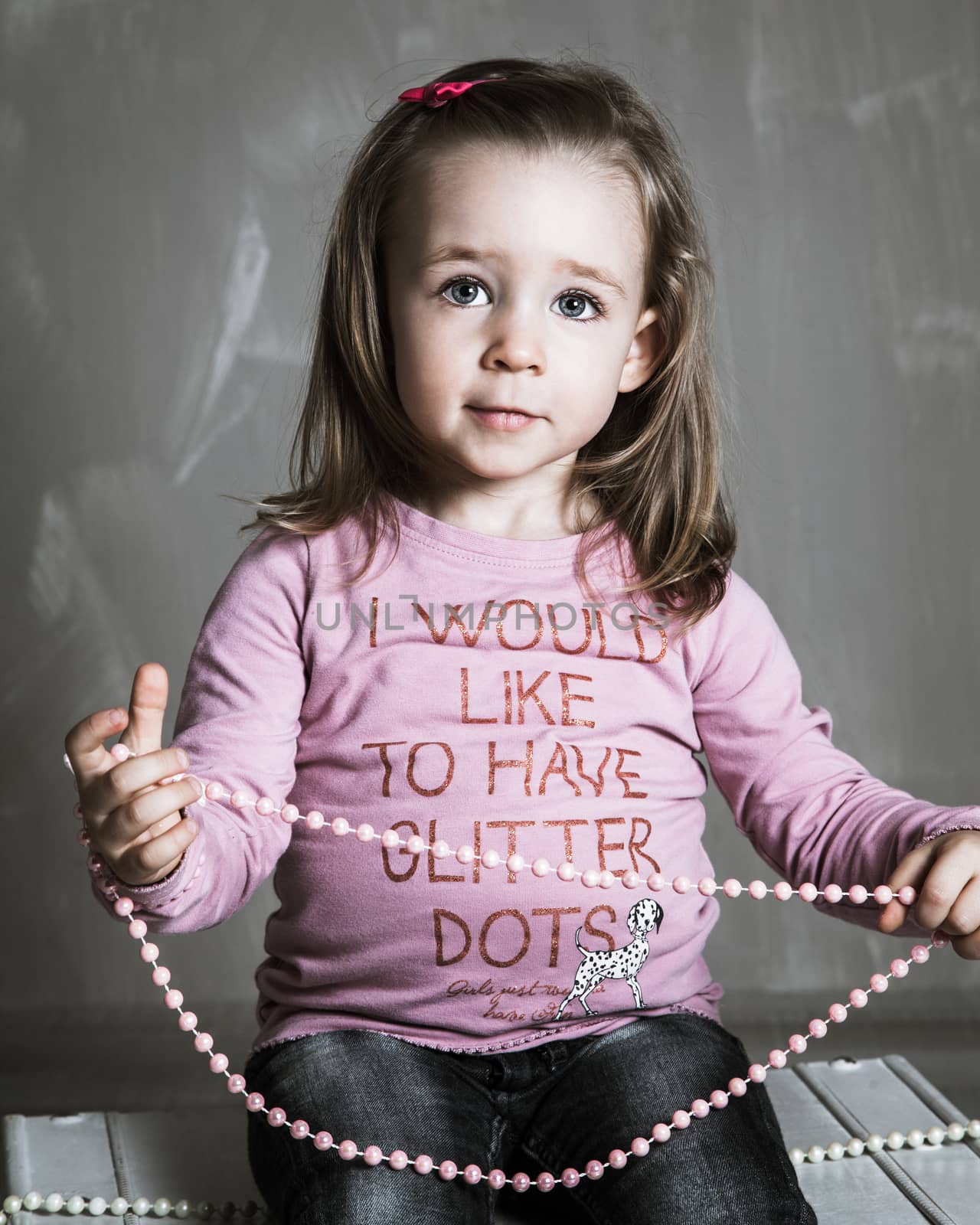 Girl playing with a pearl necklace. Image taken in the studio.