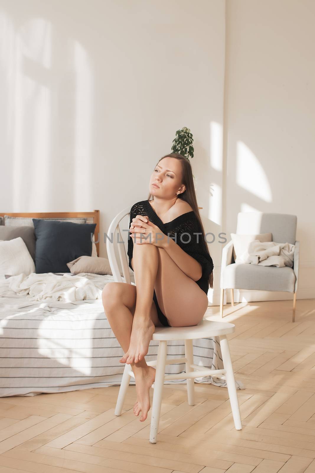 The girl is sitting on a chair, holding a hat in her hand. Girl in underwear, on heels.