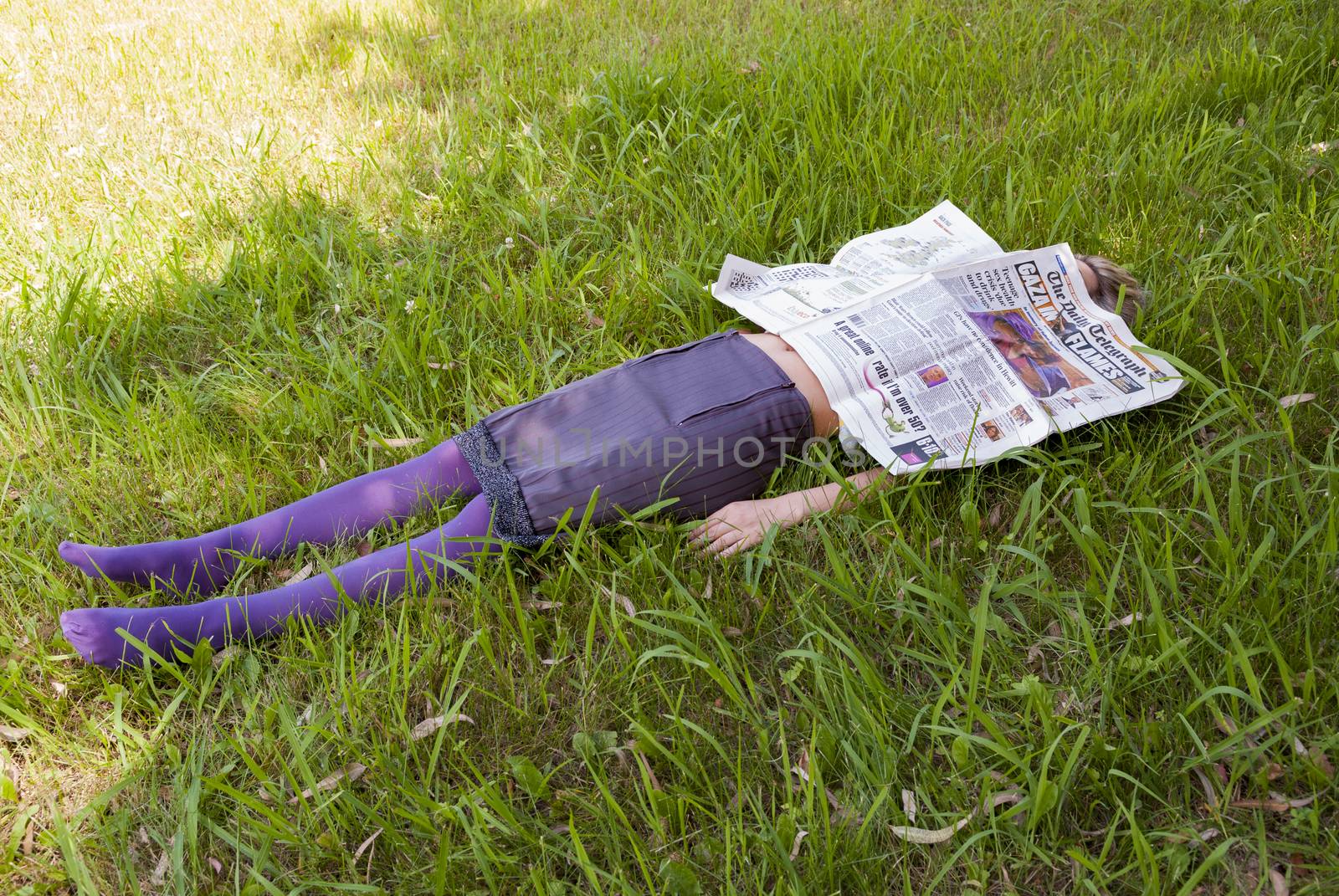 young woman lying on the grass with a newspaper in her face