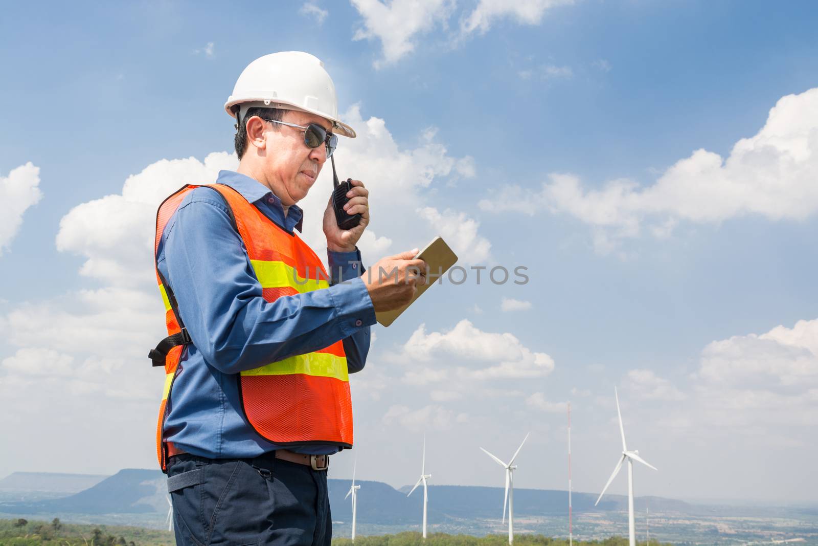 Male Architect or Engineer, use Hand-Held Transceiver Radio and Digital Wireless Tablet Device, working at Wind Turbine Power Generator Field as Infrastructure Construction Project Development