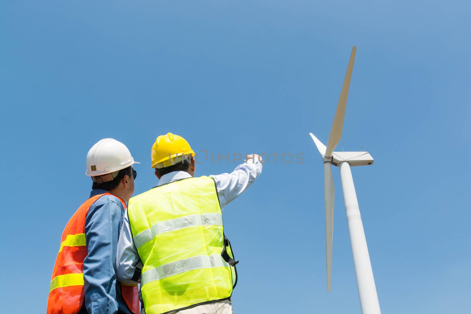 Alternative Power or Renewable Energy Technology Project Development Concept, Engineer and Architect discuss over Digital Wireless Tablet and Clipboard while working at Wind Turbine Power Generator Tower site.