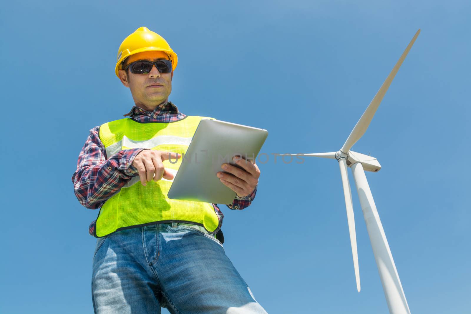 Electric Engineer use Digital Wireless Tablet Device with Wind turbine power Generator Tower Background as Green energy or Renewable Energy Technology Project Development Concept.