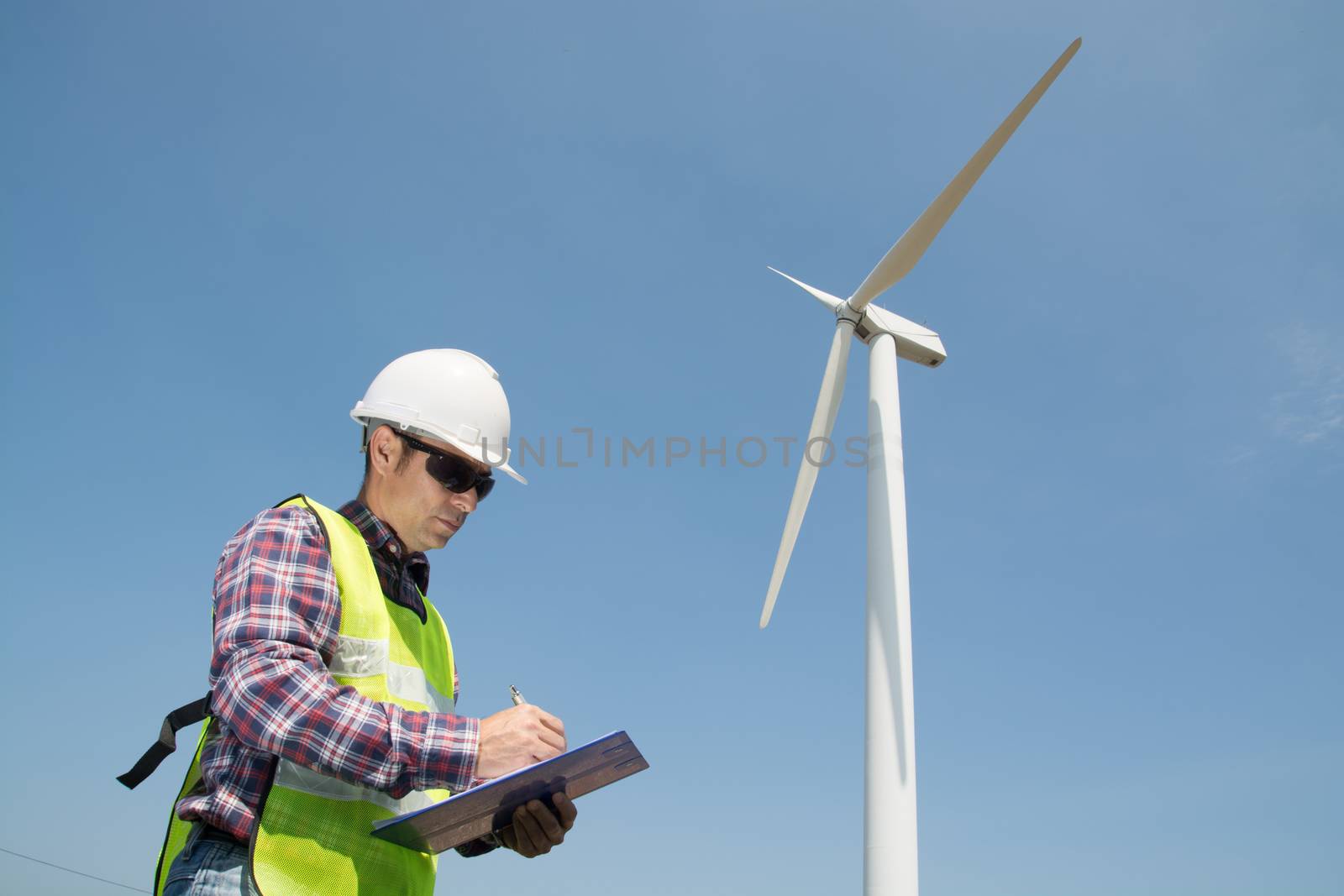 Electric Engineer writing report on Clipboard with Wind turbine  by thampapon