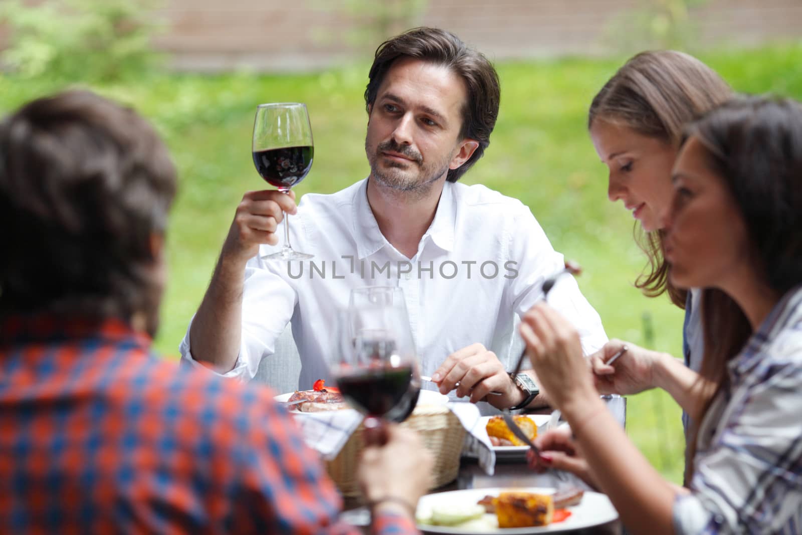 Friends clink glasses of red wine at outdoor dinner
