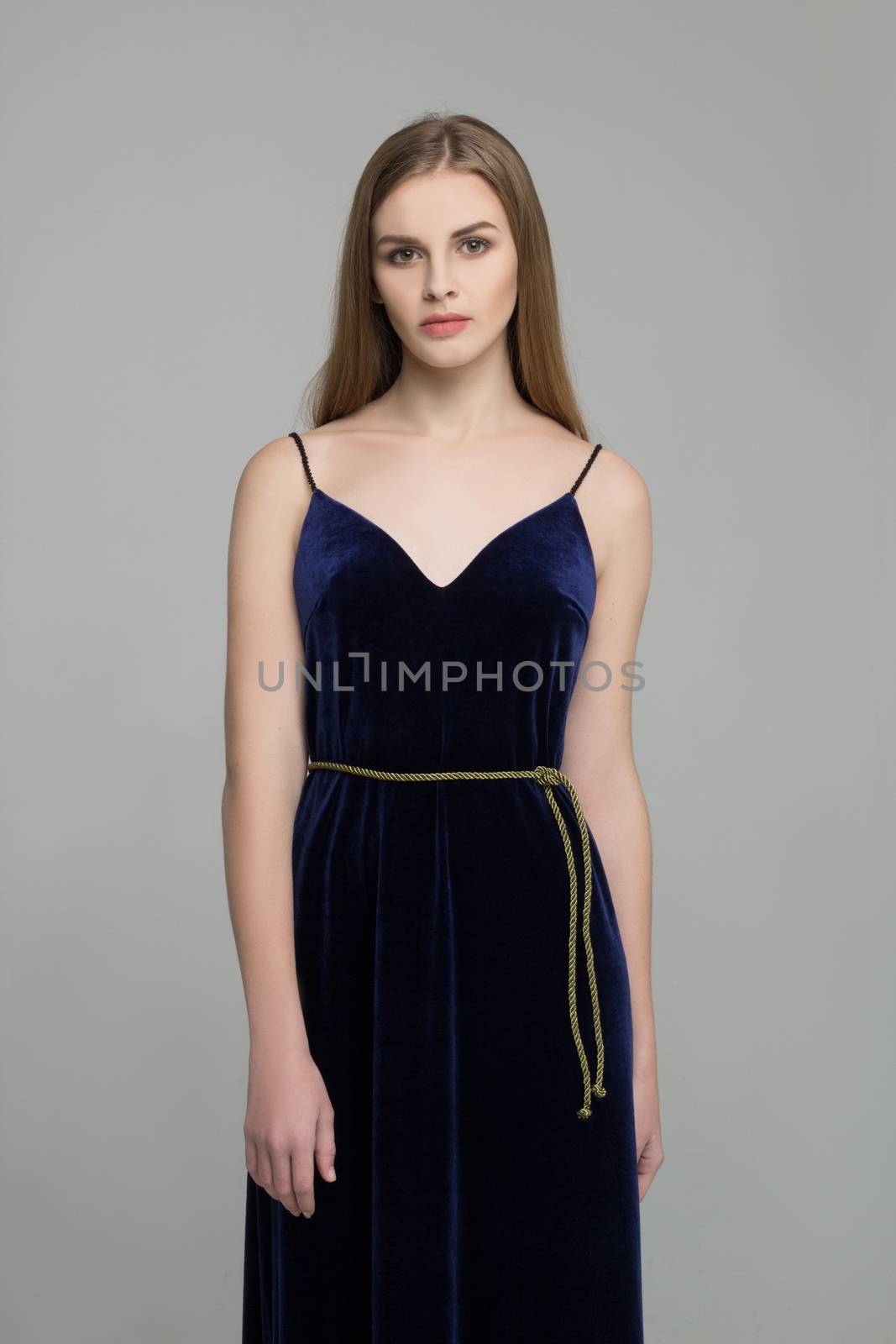 Young beautiful long-haired female model poses in long black dress on grey background