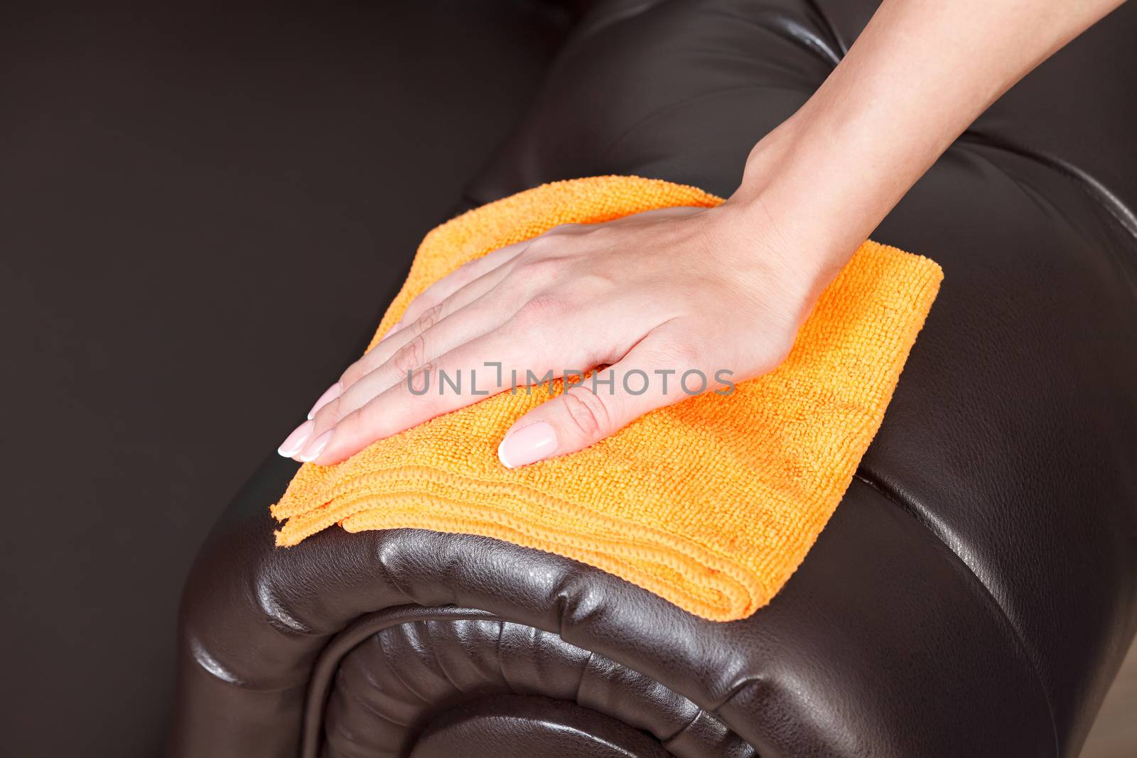 Closeup shot of female hand wiping brown leather chester couch o by Nobilior
