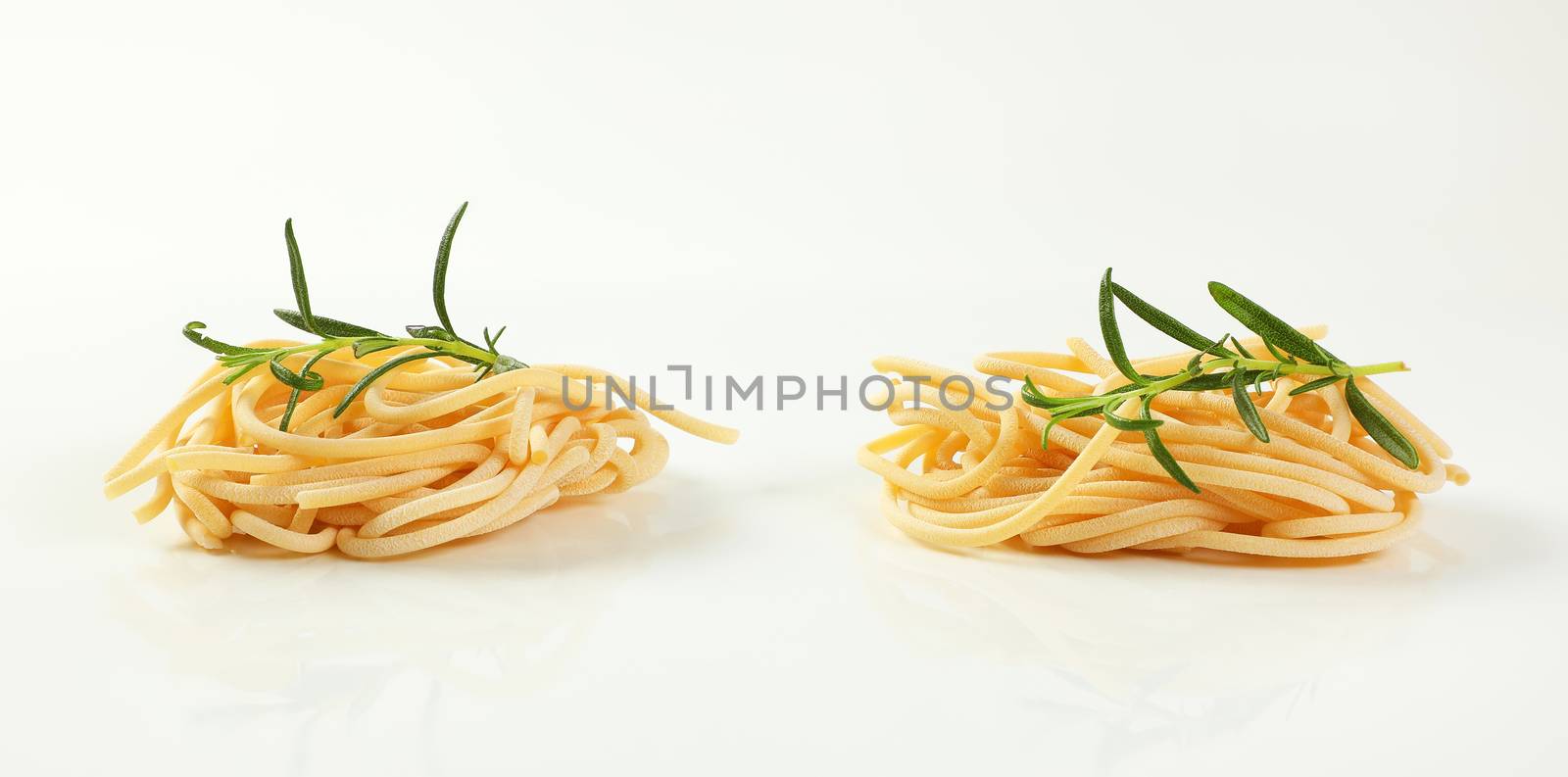 two bundles of uncooked spaghetti pasta on white background